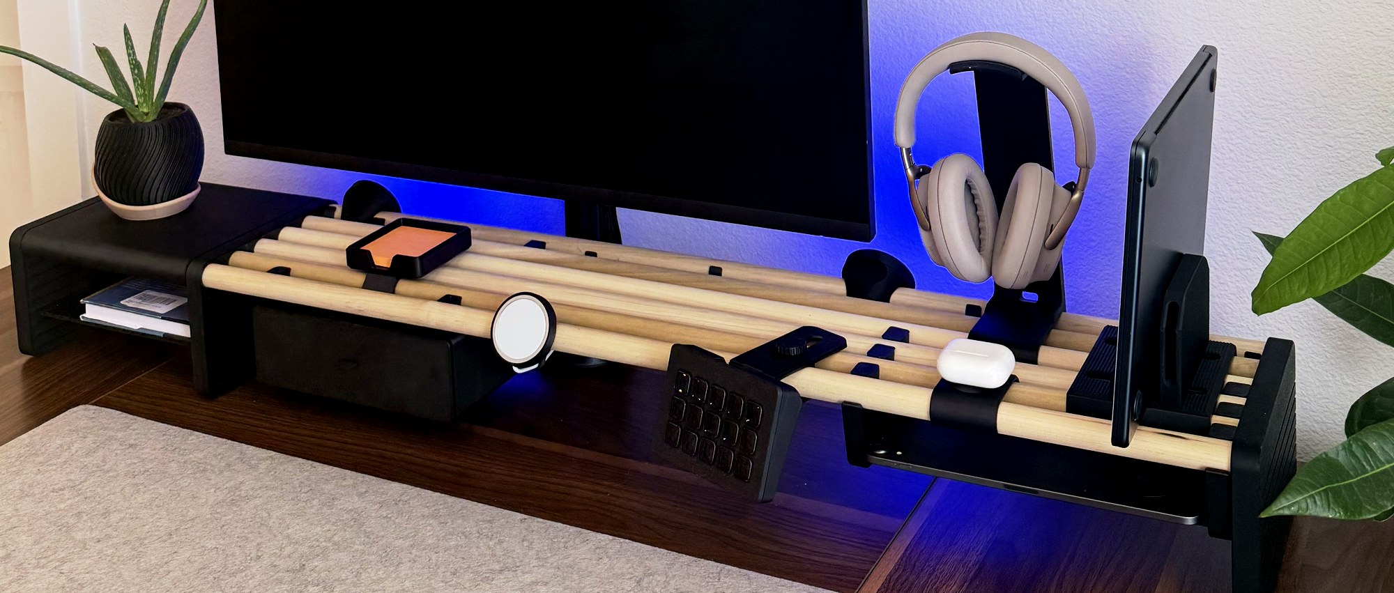 The Desk Shelf in black on a walnut desk, seen from the side with a drawer, headphone stand and tablet mount under a monitor