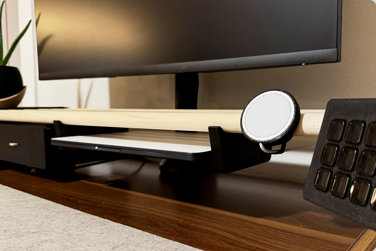 Close view of a MagSafe charger mount clamped to the wood dowels, with a sub-shelf holding a trackpad underneath